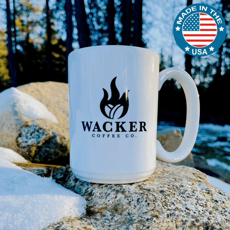 White mug with Wacker Coffee Co logo, featuring American Made Merchandise, displayed on a rock in snowy environment.
