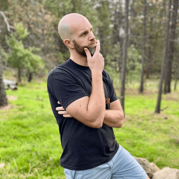 Thoughtful man outdoors in a black t-shirt contemplating choices in coffee.